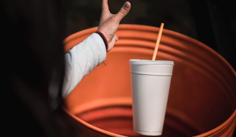 A person throwing away a styrofoam cup into the garbage