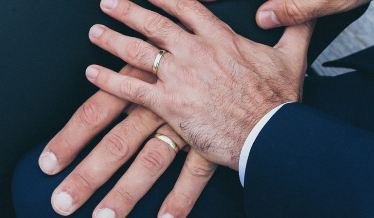 Two men's hands with rings holding each other