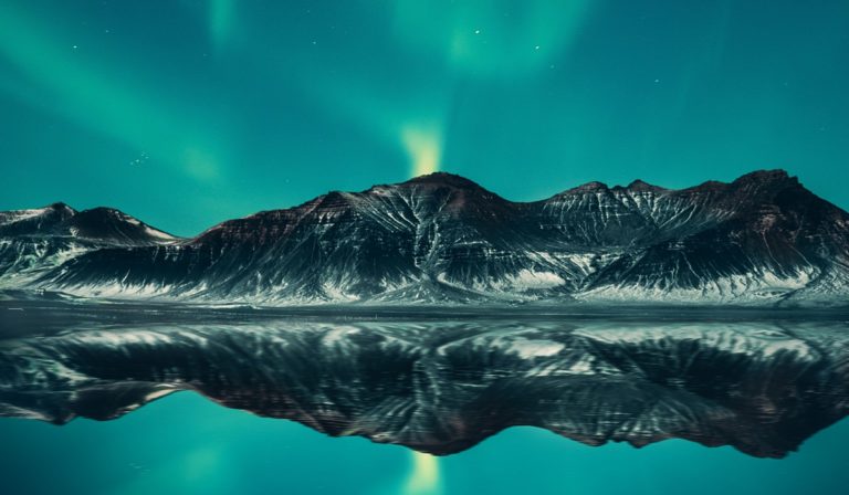 Aurora borealis above mountains reflecting in lake