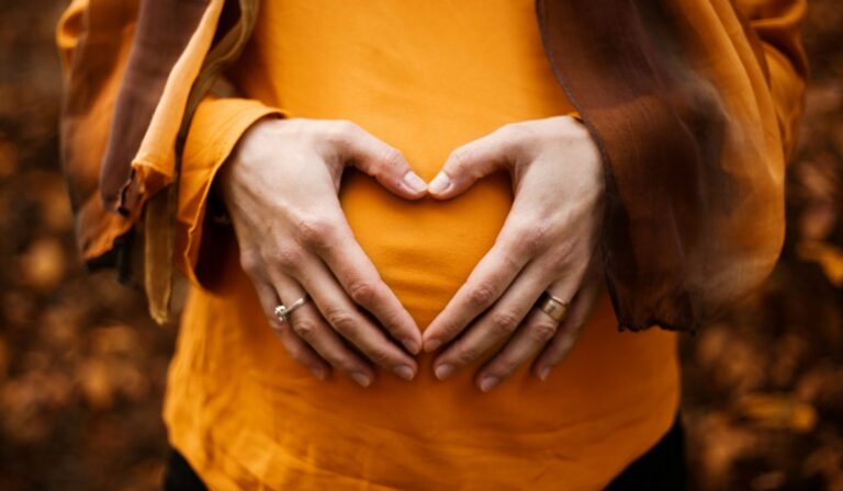Person touching pregnant belly with hands forming a heart