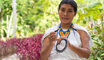 Colombian woman in traditional clothing weaving looking at the camera