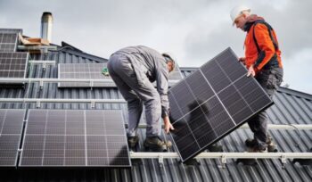 Technicians carrying photovoltaic solar module while installing solar panel system on roof of house