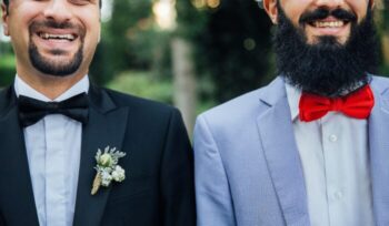 Two smiling men in wedding suits|Pride flag